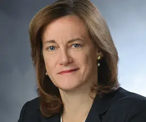 Woman with shoulder-length brown hair, slight smile, wearing a blazer, set against a neutral background.