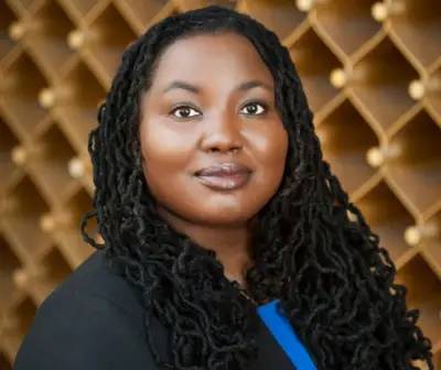 A woman with long, black dreadlocks poses confidently against a geometrically patterned background.