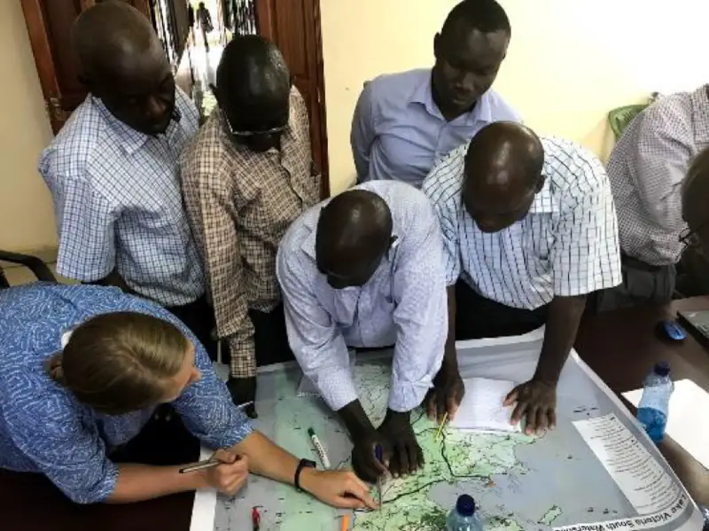 A group gathers around a map, discussing and marking locations collaboratively in an office.